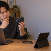 ノートPCとタブレットを前に、USB-Cケーブルや小型レシーバーを置き、マウス底面を確認する男性