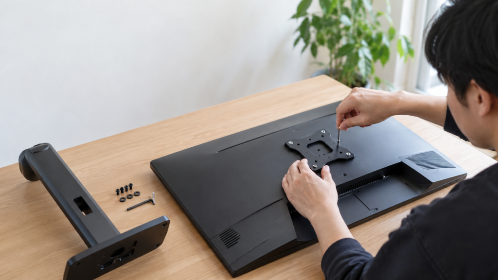 モニター背面にVESA取付プレートを合わせ、工具を使ってネジを締めているモニターアーム設置作業