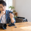 カメラとカードケースを前に、2枚のSDカードを手に取って種類の違いを見比べる男性