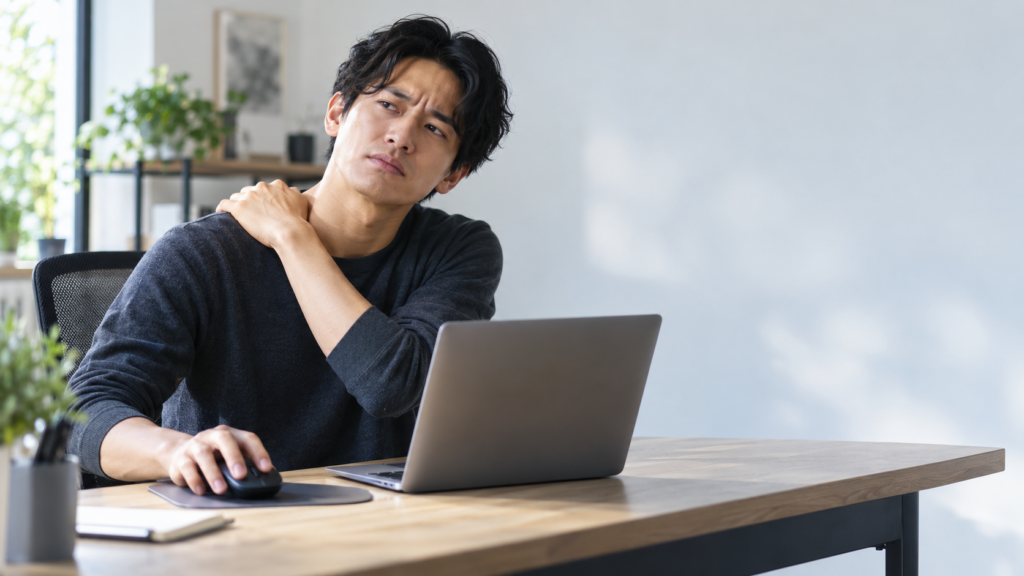 ノートPCで通常マウスを操作しながら、反対の手で肩に触れているデスクワーク中の男性