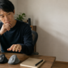 木製デスクに並んだ黒とグレーのエルゴノミックマウスを前に、手を伸ばして選び方を検討する男性