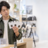 カメラ売り場で複数のSDカード候補を手に取り、使用するカメラとの組み合わせを見比べる男性