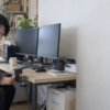 2台のモニターが置かれたデスクで、モニターアーム用クランプを手に取り設置位置を確認する男性