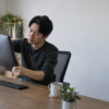 モニターアームに取り付けた画面を両手で支え、角度や位置を確認しながら調整する男性