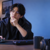 モニターを見ながら片手で多ボタンマウスを操作し、あごに手を添えて使用感を考える男性のゲーム用デスク