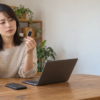 SDカードとUSBメモリを両手で見比べ、カメラやノートPCを前に保存方法を検討する女性
