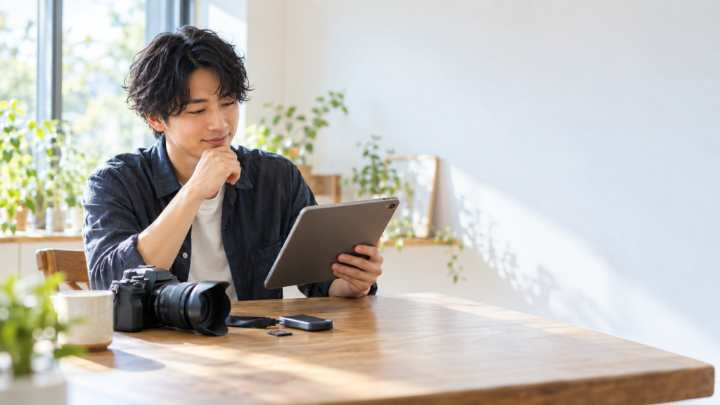 カメラとSDカード、カードリーダーを机に置き、タブレットを確認する男性