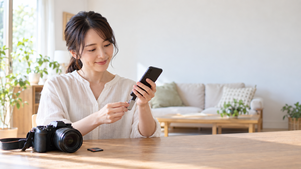 スマートフォンにUSBメモリを接続し、机上のカメラとSDカードを用途に応じて使い分ける女性