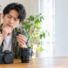ミラーレスカメラと交換レンズを置いた木製テーブルで、2枚のSDカードを手に持ち、それぞれの違いを見比べる男性