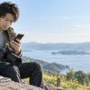 撮影先でカメラを下げた男性がスマートフォンを確認し、そばにSDカードケースを置いている